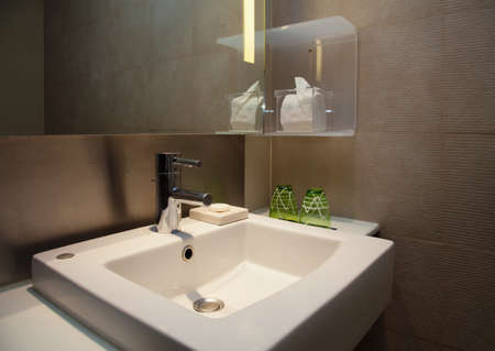 Modern restroom with steel water faucet and square white sink beneath illuminated mirror.の写真素材
