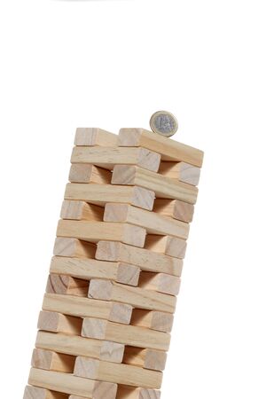 toy wooden blocks tower with a 1 euro coin on the top inclined until falling isolated on white background with copy spaceの写真素材