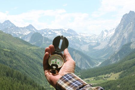 man hand holding an orientation compass with beautiful mountain scenery on the background with copy space for your textの写真素材