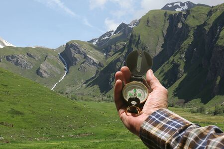 man hand holding an orientation compass with beautiful mountain scenery on the background with copy space for your textの写真素材