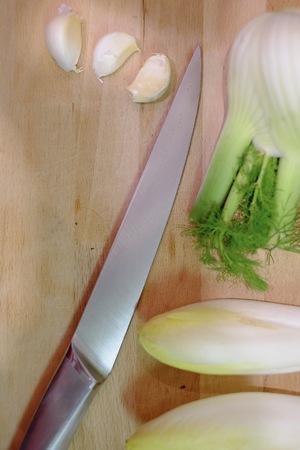 Kitchen knife and vegetables on a wooden cutting board in the kitchen, preparing and cutting the vegetables while cooking a healthy meal with garlic, fennel and chicoryの写真素材