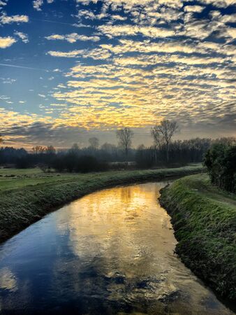 Sunset sky with altocumulus clouds reflected in the water of the riverの写真素材