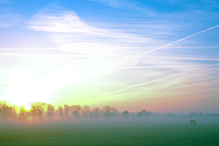 Natural sunset or sunrise over a field or meadow with a bright and dramatic sky and dark ground at the countrysideの写真素材