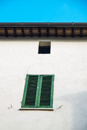 Green window and blinds outside a weathered facade of a white home in Montone Italyの写真素材