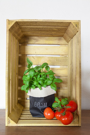 Fresh ripe garden tomatoes and basil on wooden background of a wooden crate with copy spaceの写真素材