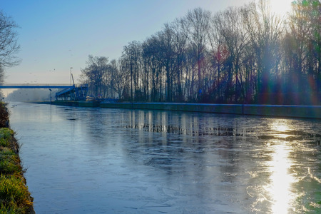 Beautiful early winter landscape with a frozen river or canal, treelined riverside and grass at sunrise creating a tranquile and quiet scenic nature backgroundの写真素材