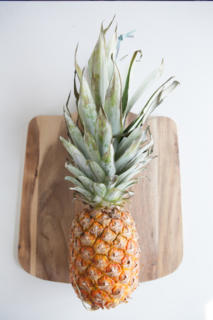 A pineapple in a flat lay layout on a wooden cutting board against a white backgroundの写真素材