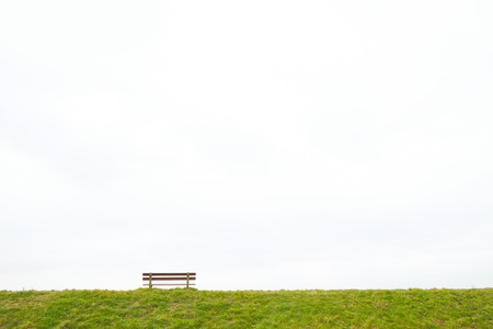 A single empty wooden bench on the horizon above a grass field against a large grey clouded sky...