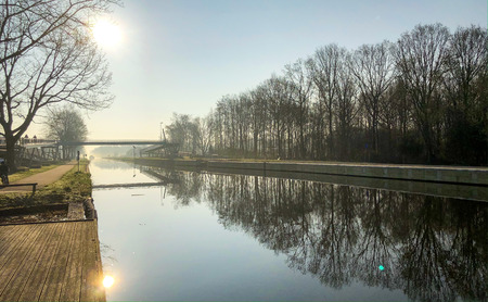 Dramatic and colorful sunrise or sunset over a beautiful landscape with a river or canal, treelined riverside and grass at sunrise creating a tranquile and quiet scenic nature backgroundの写真素材