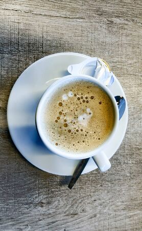 Fresh cup of coffee with a spoon and an empty cup of creamer on the saucer plateの写真素材
