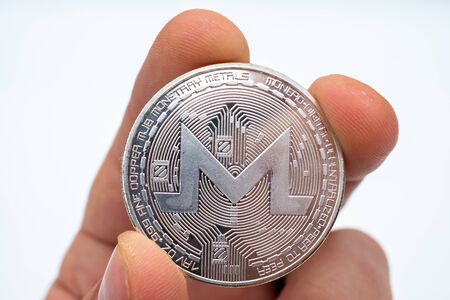 Hand holding a Monero cryptocurrency coin in his hand against a white backgroundの写真素材
