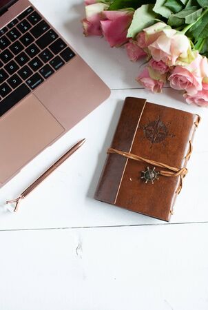 Womens workspace with laptop, bouquet of pink roses, a notebook, a pen and a cosy blanket in a flat lay top viewの写真素材