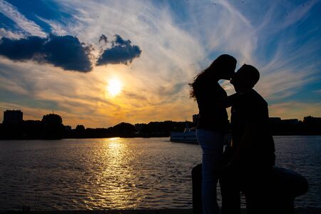 Silhouette of a loving couple cuddling during a golden sunset reflected in the water, showing the concepts of love, couple, romance, valentine, togethernessのeditorial素材
