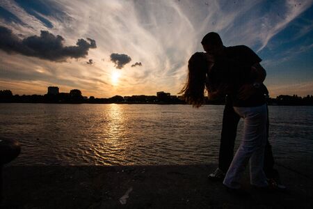 Silhouette of a loving couple cuddling during a golden sunset reflected in the water, showing the concepts of love, couple, romance, valentine, togethernessのeditorial素材
