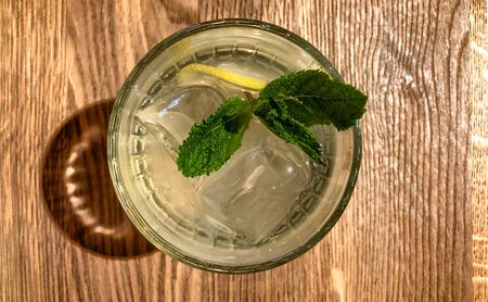 A glass of lemon mint water and fresh mint leaves on a wooden tableの写真素材