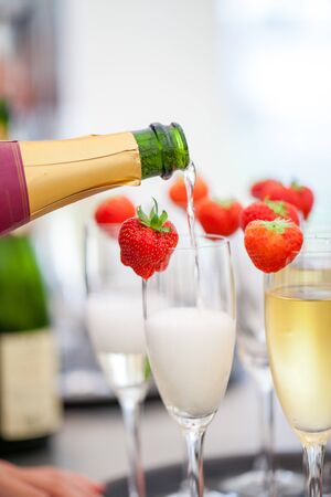 Sparkling wine or champagne and strawberry on a blurry background being poured out from the bottle during some sort of festivity or celebration such as a wedding, borthday or newyearの写真素材