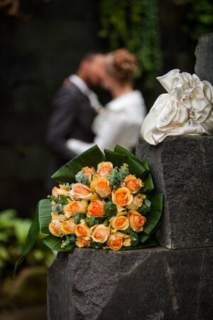 Beautiful interracial newlywed couple kissing out of focus in the background with the colorful bridal bouquet in the frontの写真素材
