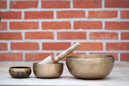 Ancient hand crafted traditional Tibetan meditation and healing singing bowls made from 7 sacred metals which are typical accessories used in buddhism, yoga and meditation, against a red brick wallの写真素材