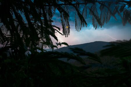 Dramatic sunset dusk sky in a mountainous landscape seen from behind palm leaves.