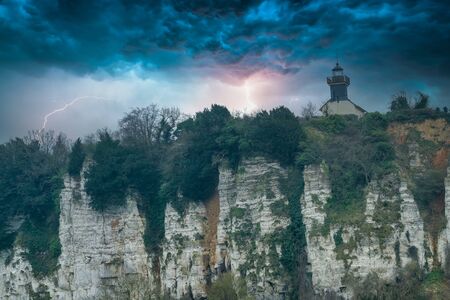 Lighthouse on a chalk cliff under a dramatic thunderstorm sky in Normandy, Franceの写真素材