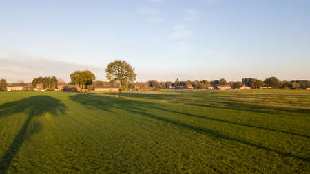 Dramatic and colorful sunrise or sunset sky over a grassy green farmfield shot from drone high up. High quality photoの写真素材