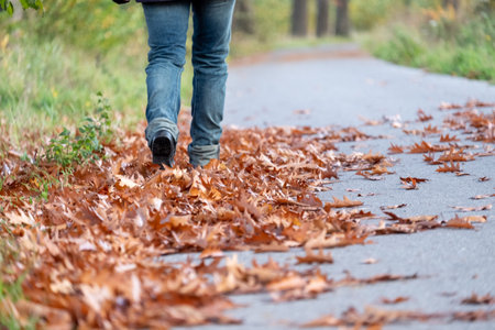 Feet trekking boots hiking through fall foliage. Traveler alone outdoor wild nature. Woman walking...