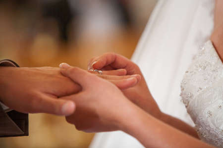 Closeup of bride putting a wedding ring onto the grooms finger. Couple exchanging wedding rings. High quality photoの写真素材