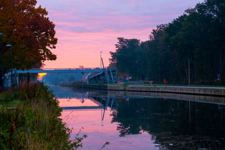 River stream canal and a bridge with grass banks and wild flowers and trees in a scenic landscape on a misty autumns morning sunrise day. High quality photoの写真素材