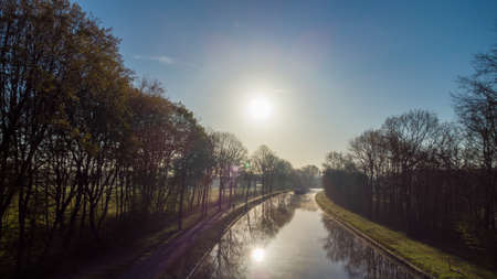 Aerial view of an Idillic river stream canal with grass banks and wild flowers and trees in a scenic landscape on a misty sunny spring morning sunrise day, taken with a drone. High quality photoの写真素材