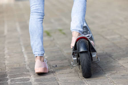 Close-up of female feet of a girl wearing pink sneakers and a jeans on electric kick scooter on the...