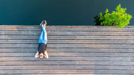 Vacation, enjoyment and freedom concept. Top aerial view from drone lifestyle portrait of young woman on a wooden riverside next to the water of the river. High quality photoの写真素材