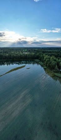 Aerial panorama view of a beautiful and dramatic sunset over a forest lake reflected in the water,...