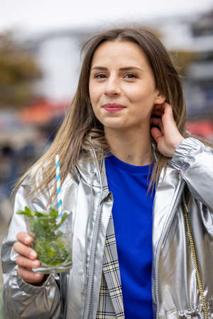 Attractive young woman or twentysomething girl drinking mojito with straw in city center during...