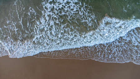 Aerial drone view perpendicular to the blue waves crashing on the sandy beach at the coast. The...