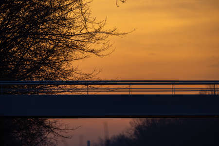Detail of the long hanging pedestrian bridge or footbridge over the canal in Rijkevorsel, Antwerp, Belgium, against an orange dramatic sunrise sky in wintertime. High quality photoの写真素材