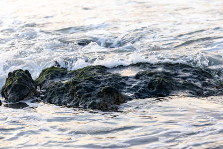 Breaking waves to the large rocks on shore creating some white sea foam and small bubbles, with a...
