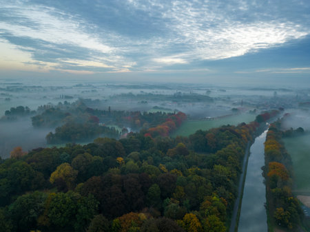 Aerial view of foggy trees in field at colorful sunrise in autumn. Colorful landscape with forest in low clouds, river, meadow in fog, orange sky with sun in the morning in fall. Top view. Nature. High quality photoの写真素材