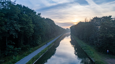 Aerial view, shot by a drone, of the sun rising or setting behind the river and fills the trees with warm evening light, fog rises in the rays of golden light. Clouds and clouds are reflected in the water. river Ob. High quality photoの写真素材