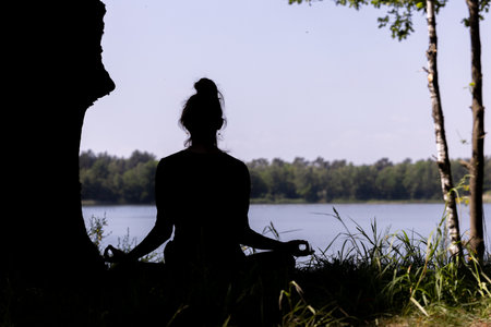 silhouette of a woman who practices yoga and meditates in the lotus position in nature. High quality photoの写真素材