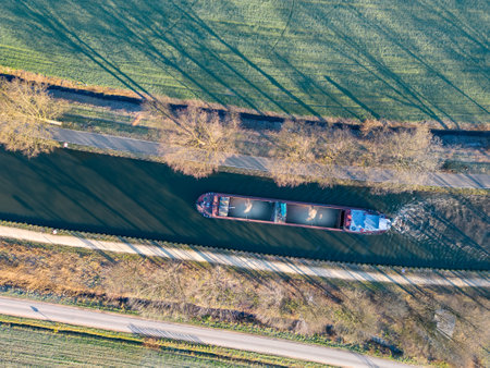 Aerial view from a drone of a cargo canal ship passes by over the canal on a sunny winter day, reflections are to be seen in the water, canal system in the outskirts of Rijkevorsel, Belgium. High quality photoの写真素材