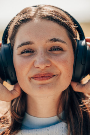 Face of pretty young woman listening to music with wireless headphones outside in nature. Woman with wireless headset on her ears. High quality photoの写真素材