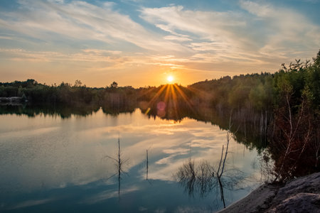 Beautiful landscape with colorful sunset over forest lake, Epic red and golden clouds above the...