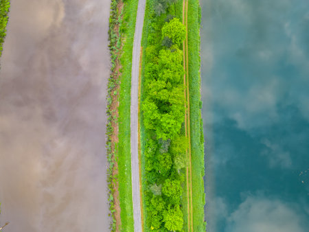 Top view or aerial view of a canal and a river next to eachother through a sunny rural landscape in spring, with a landslide with green, tree and dirt roads in between. High quality photoの写真素材