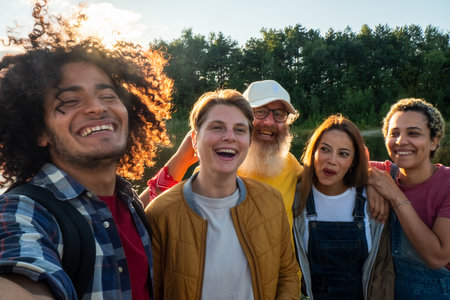 A joyful moment as a multiracial group of trendy millennial friends enjoys vacation, capturing memories with a selfie on a forest lake beach - celebrating friendship and free time. Diverse Friends Taking Selfie on Lake Beach. High quality photoの写真素材