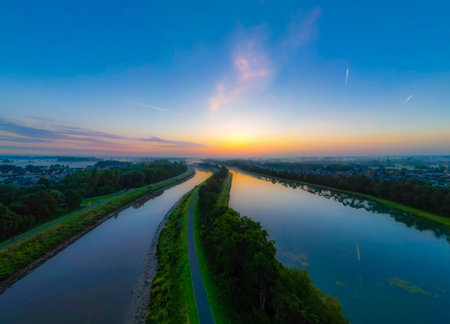 Capture the serene beauty of dawn as the sun peeks under a steel-blue sky, its golden rays reflecting off two tranquil waterways, creating a breathtaking spectacle of nature.Dawns Reflection: Sunlit Waterways Under Steel Sky. High quality photoの写真素材