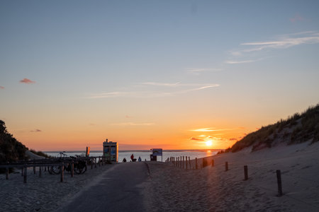 The image features a sandy path leading to a beach bathed in the warm hues of a sunset. Silhouettes...