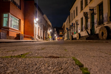This image captures the essence of a late evening in Lillo, Antwerp, with the cameras low perspective emphasizing the cobblestone texture. The historic towns charm is illuminated under the soft glow of streetlights, casting warm hues on the facades of buildings and the quiet streets. A sense of stillness pervades, inviting contemplation of the towns rich history and the stories embedded in its architecture. The street leads the eye toward the heart of Lillo, with the ambient light creating a pathway through the night. Cobblestone Quietude: Lillos Nocturnal Streets. High quality photoの写真素材