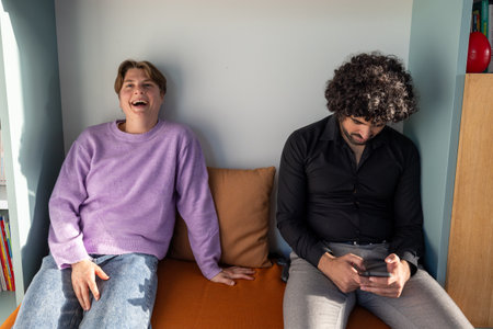 A man wearing a black shirt sits beside a woman in a purple sweater, sharing a moment of comfort and leisure as they engage in an event or fun activity togetherの写真素材