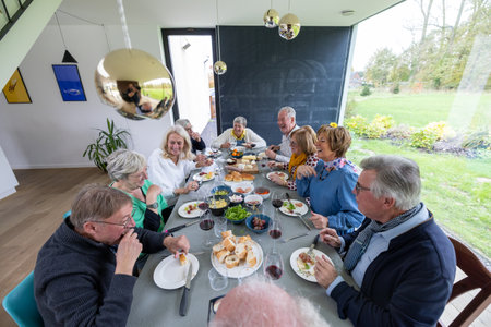 A warm gathering of family and friends enjoying a meal in a bright, modern home, filled with happiness and laughterの写真素材