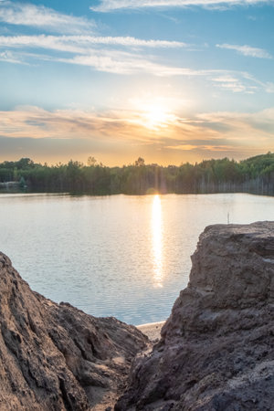 The sunset creates a stunning scene on a calm lake, with rocks in the front and a peaceful forest in the backの写真素材